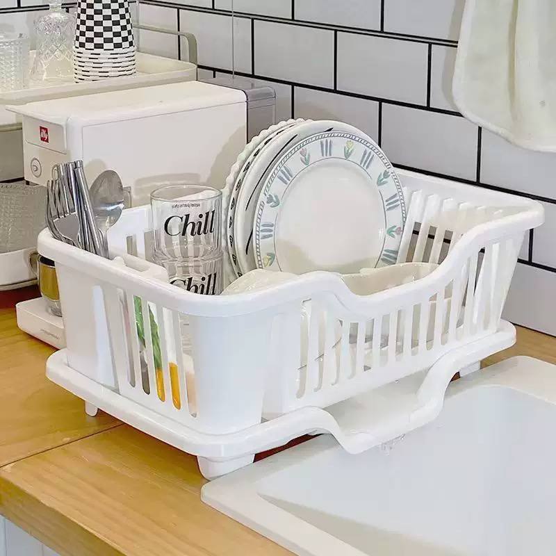 White dish drying rack with drain tray holding plates and cutlery on a kitchen counter